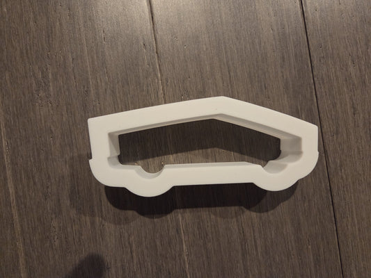 White Cybertruck-shaped cookie cutter lying on a dark wood surface. Made in Indiana