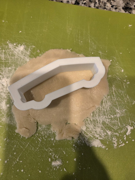 Cybertruck-shaped cookie cutter pressed into rolled cookie dough on a floured mat