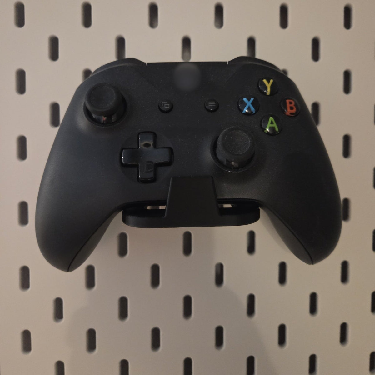 Black game controller holder on a pegboard holding a black controller