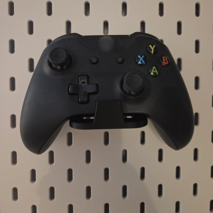 Black game controller holder on a pegboard holding a black controller