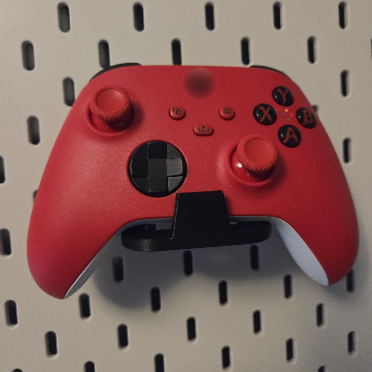 Black game controller holder on a pegboard holding a red controller