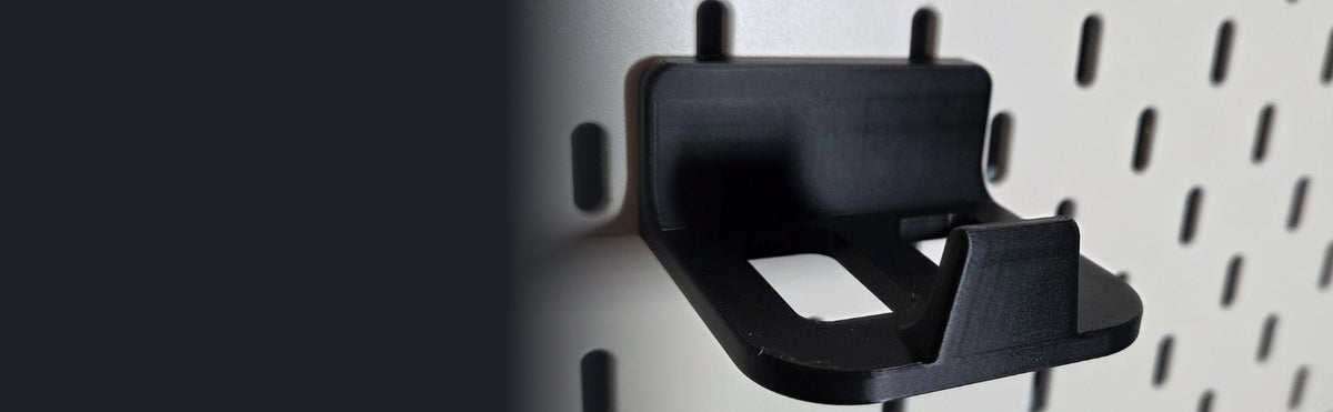 Black game controller holder mounted on a white pegboard for desk organization