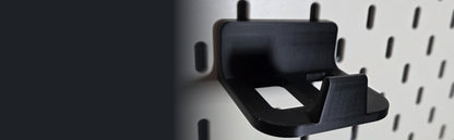 Black game controller holder mounted on a white pegboard for desk organization