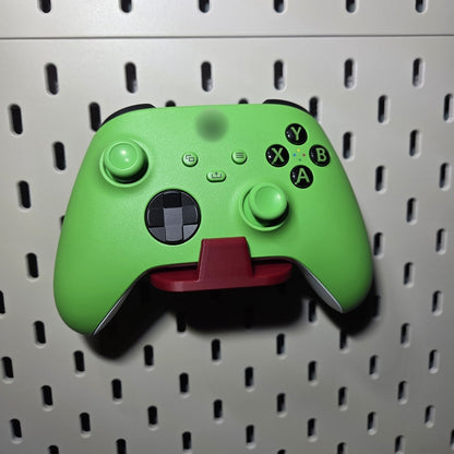 Red game controller holder on a pegboard holding a green controller