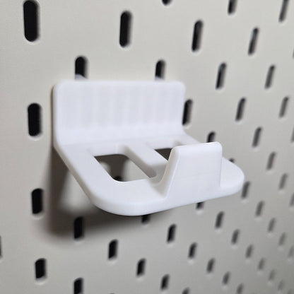 Close-up of the white controller holder hooked into a pegboard, open tray with raised front lip