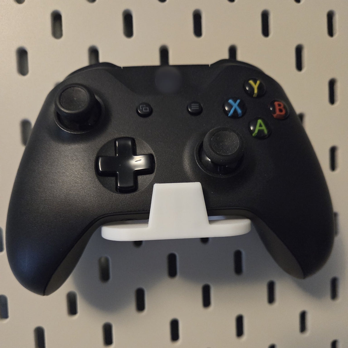 White game controller holder on a pegboard holding a black controller
