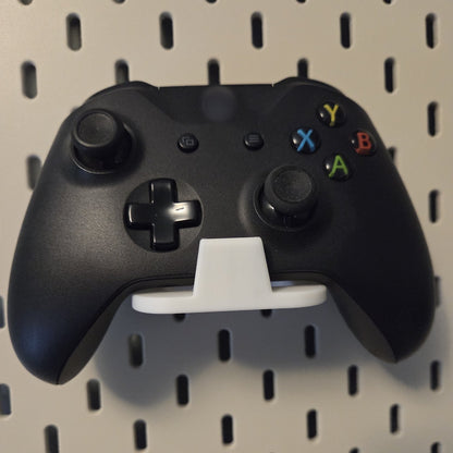 White game controller holder on a pegboard holding a black controller