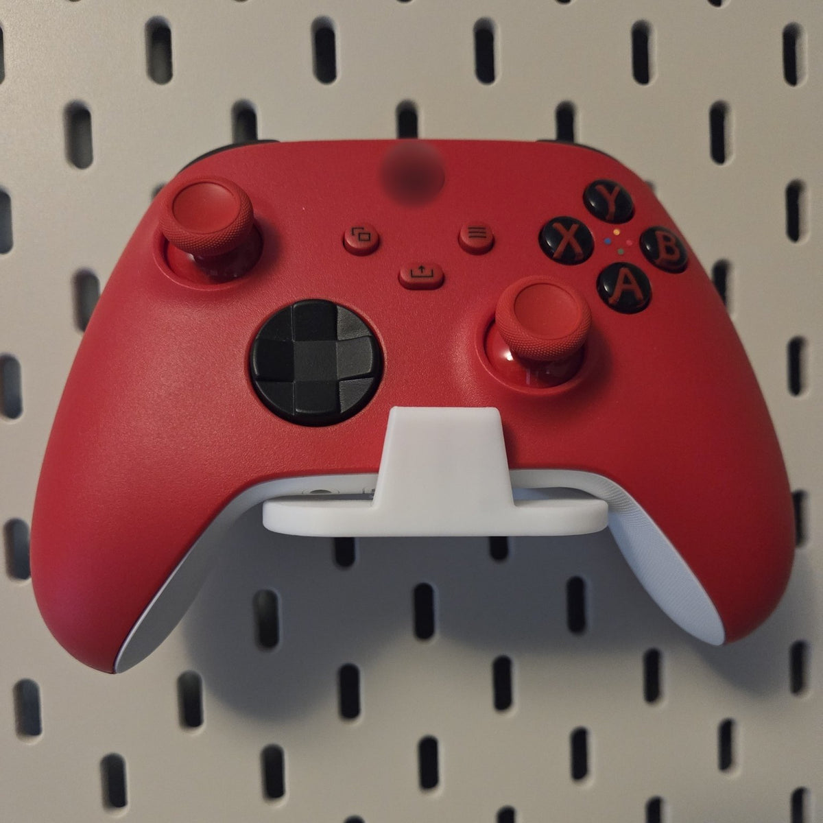 White game controller holder on a pegboard holding a red controller, compatible with IKEA SKADIS